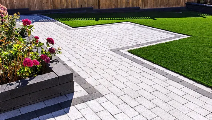 Light grey paver patio with a dark border and planter wall by NewStone
